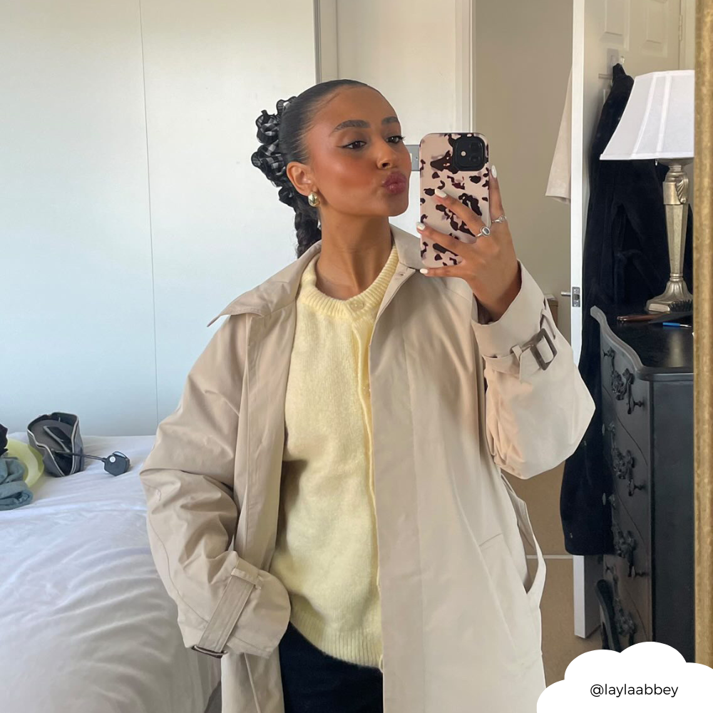 Woman in beige trench coat and yellow sweater holds ivory tortoiseshell Coconut Lane Tough Phone Case in mirror selfie.