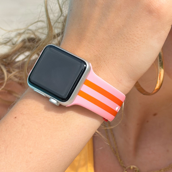 Person wearing a Apple Watch with a Orange and Pink Watch Strap on a beach.