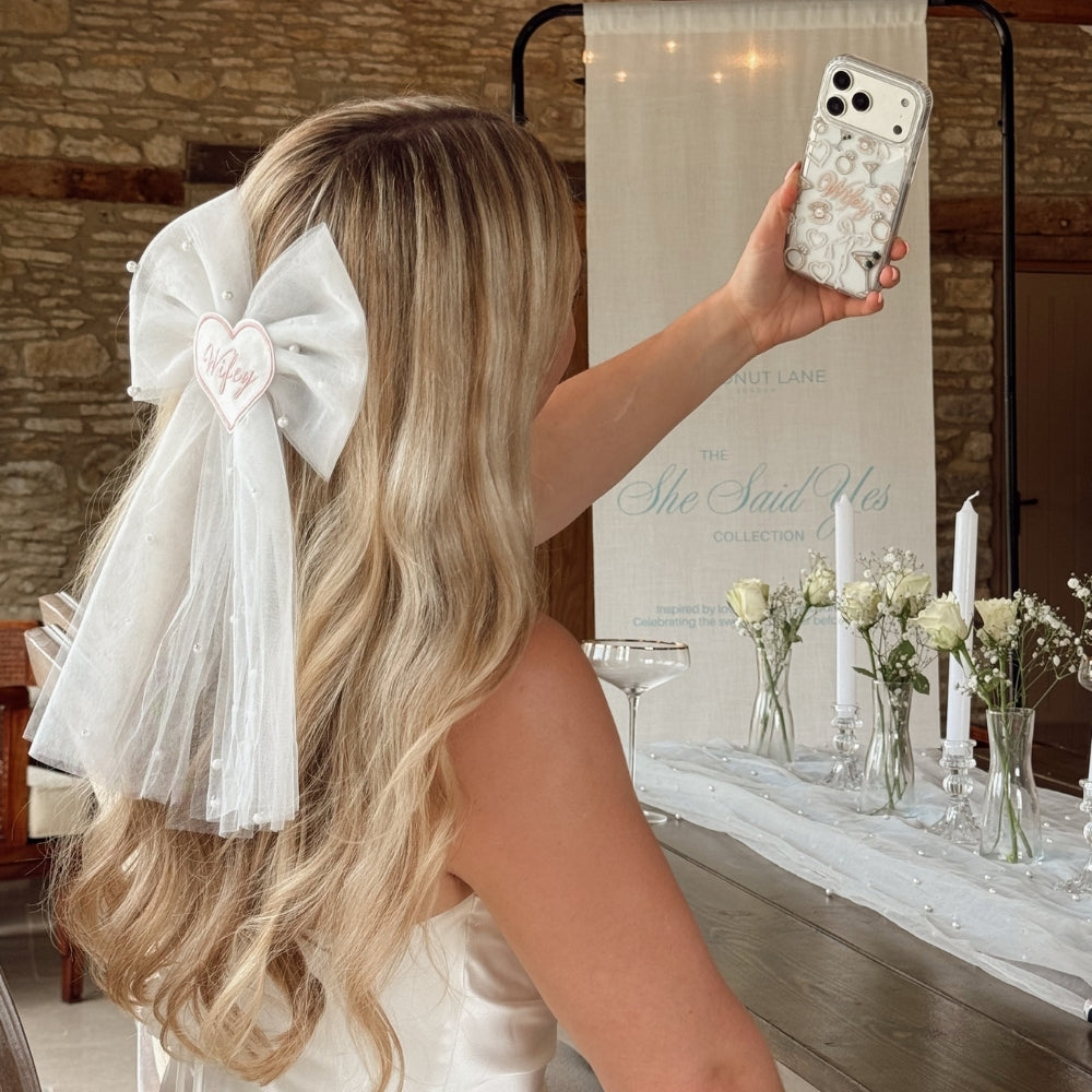Bride to be with a large white bow in her hair which says 'wifey' taking a selfie.