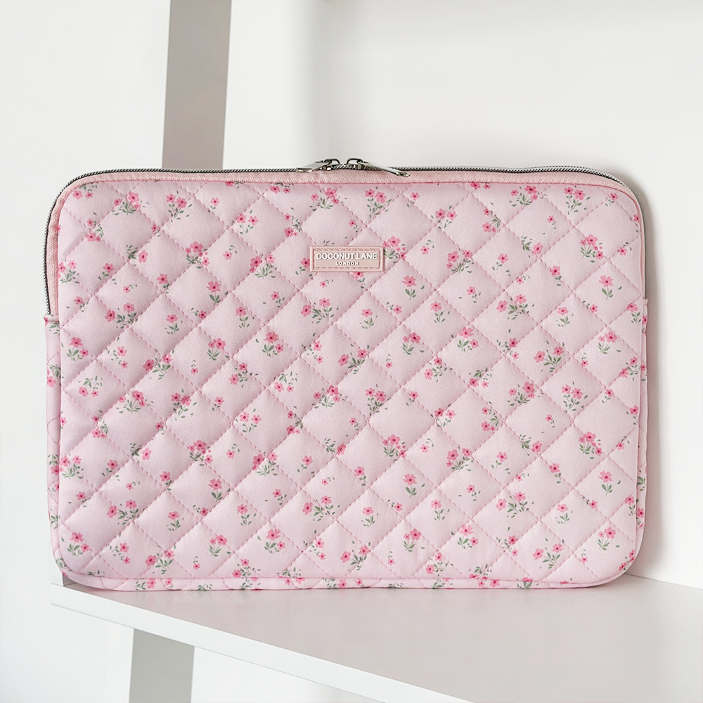 Pink quilted laptop sleeve with ditsy floral pattern, standing upright on a white shelf.