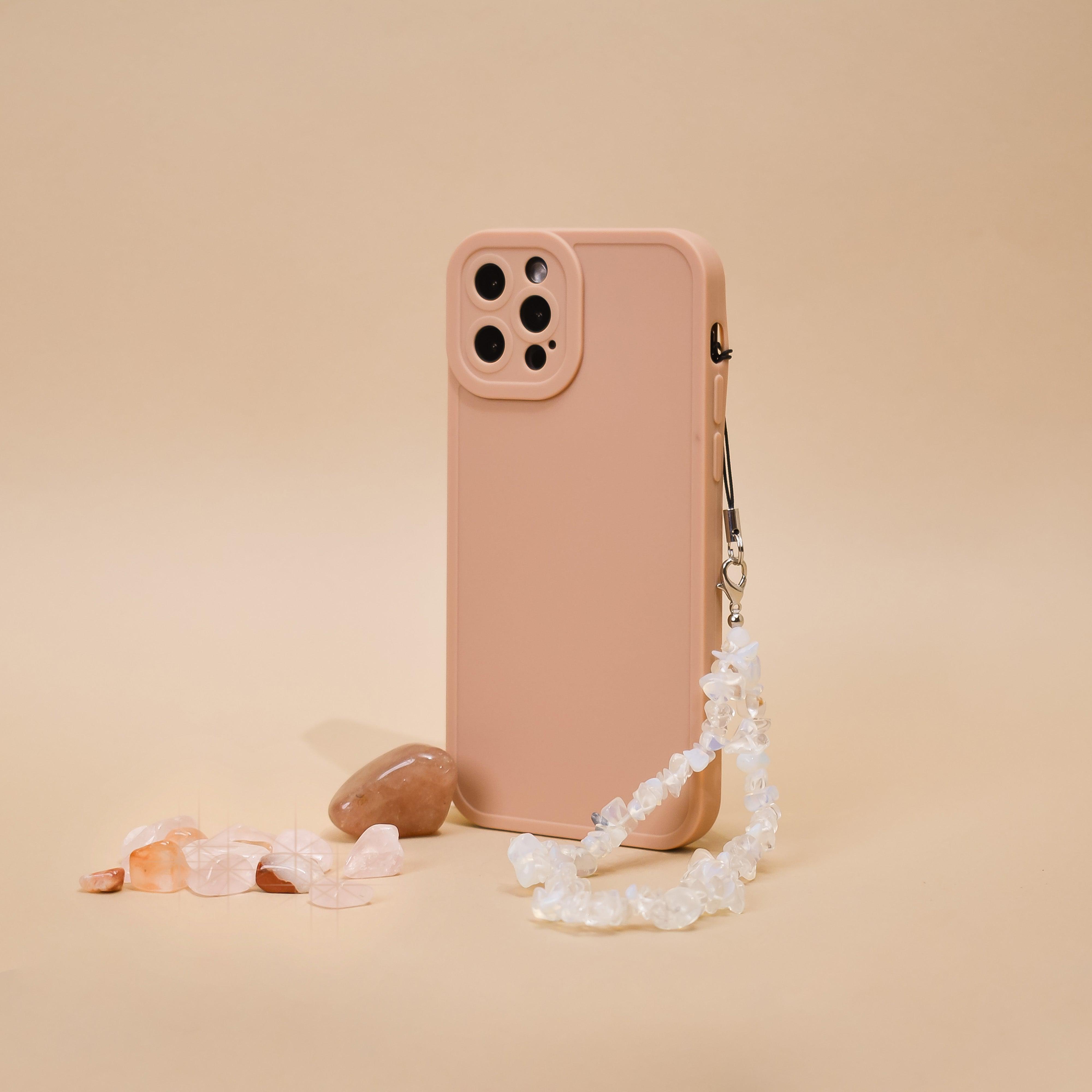 Moonstone crystal phone strap by Coconut Lane on a pink phone case, next to polished stones on a beige surface.