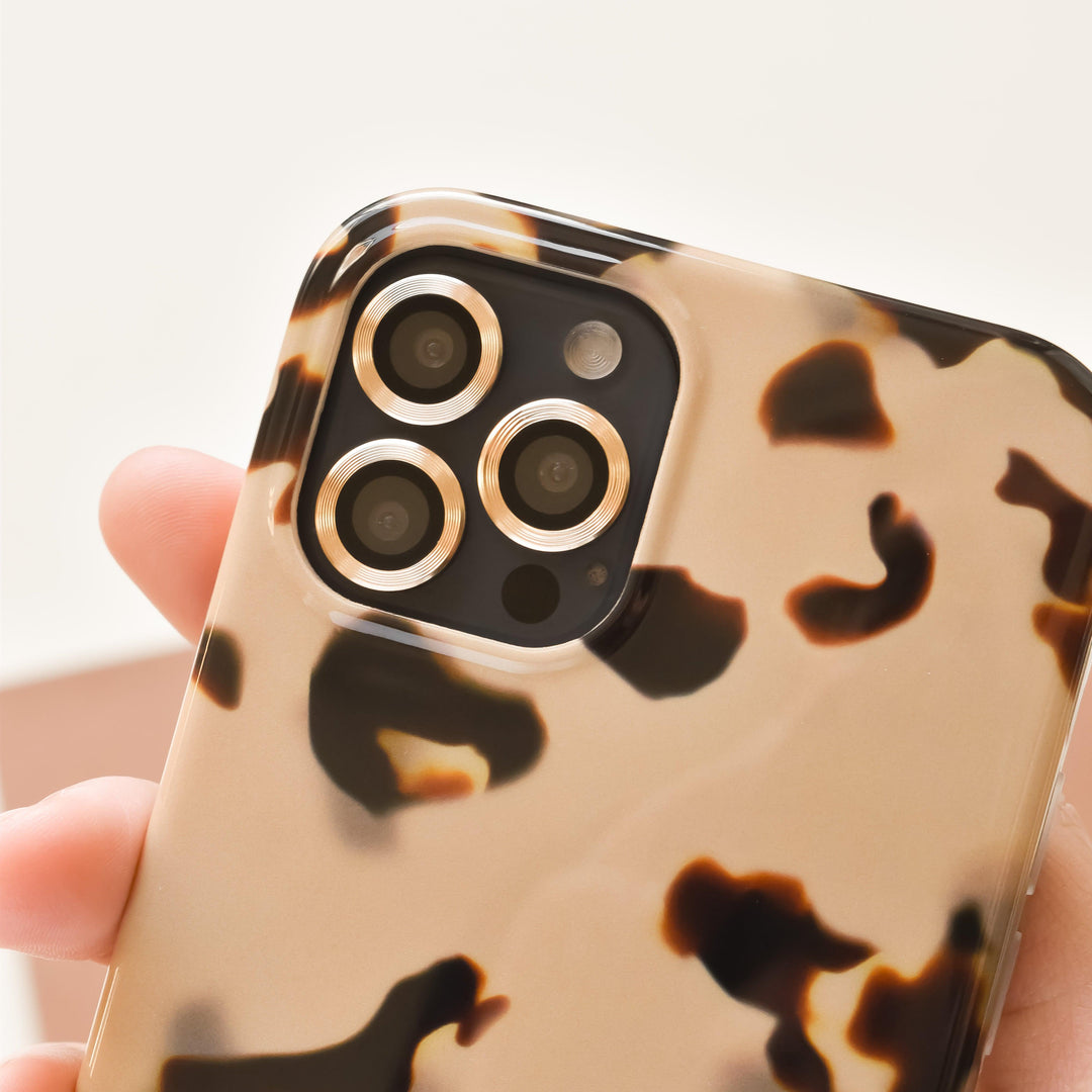 A hand holds a smartphone with a camera featuring three lenses. The phone is encased in a brown and beige tortoiseshell patterned case, providing a stylish and trendy appearance.