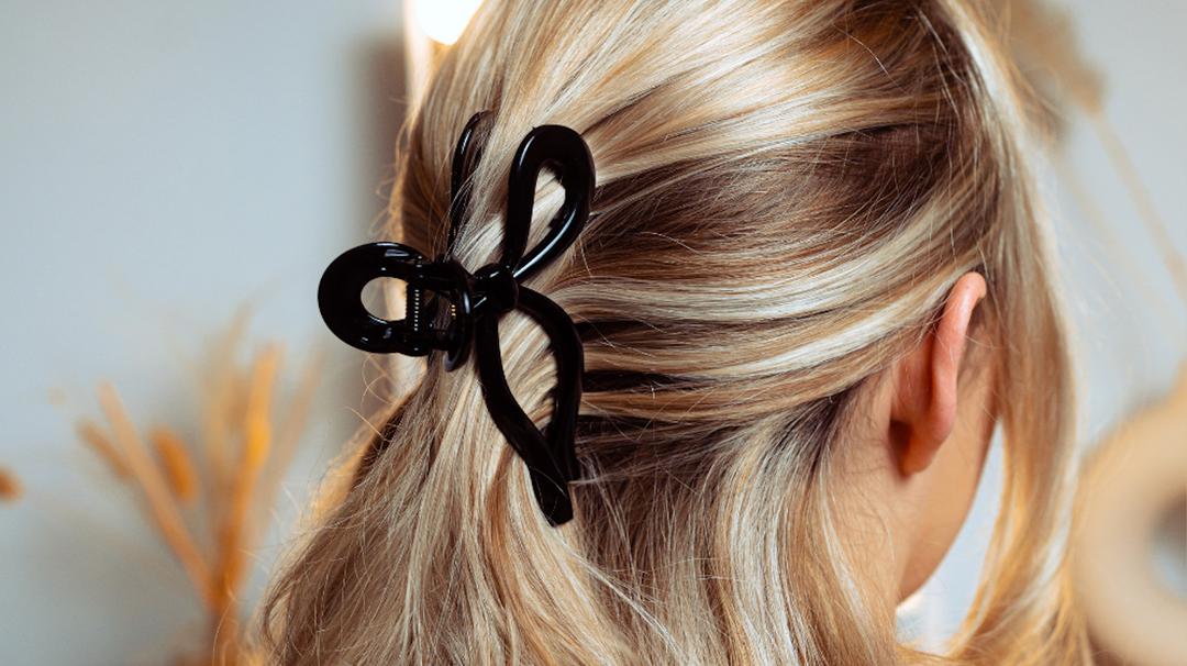 A person with blonde hair styled in a half-updo secured with a large black hair clip shaped like a bow.
