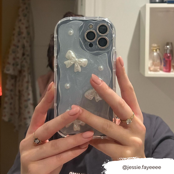 A person with neatly manicured pink nails holds a Pearls & Bows Phone Case from Coconut Lane, featuring a protective clear design embellished with white bows and pearls. The background reveals a blurred bathroom scene with shelves and hanging robes. The Instagram handle @jessie.fayeeee is overlaid on the bottom right corner.