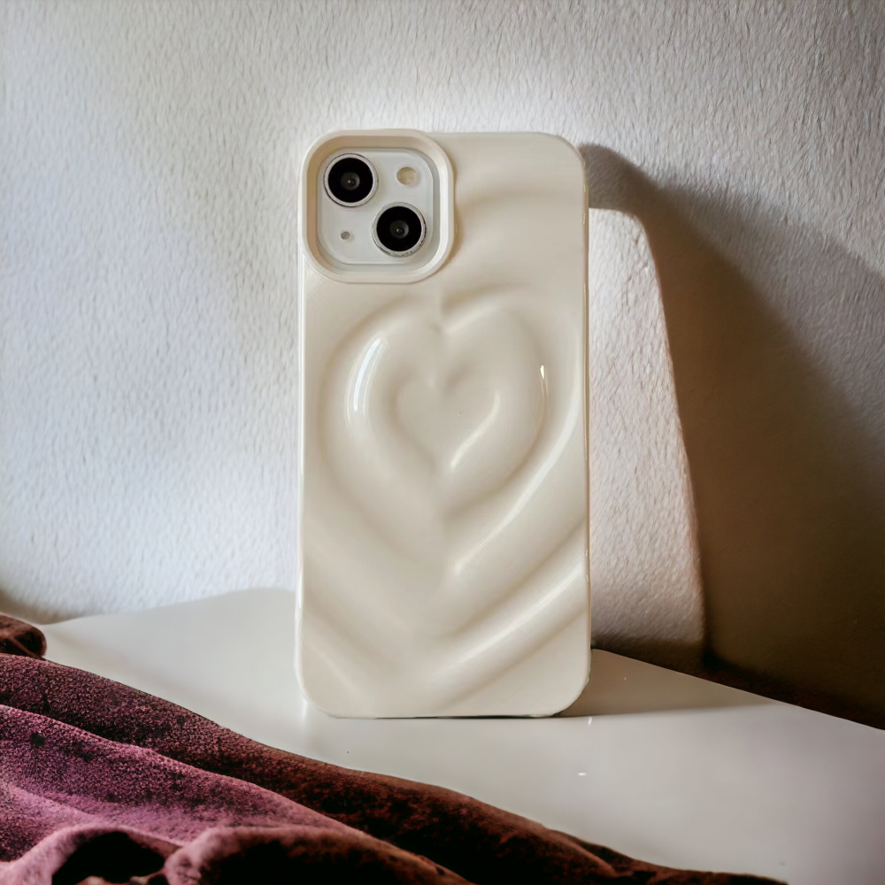 A white smartphone with a Melting Heart Phone Case - Coconut Cream by Coconut Lane stands upright on a white surface. A reddish-purple fabric is visible in the foreground, casting shadows. Light enters from the right, illuminating the phone and casting a shadow on the wall behind.