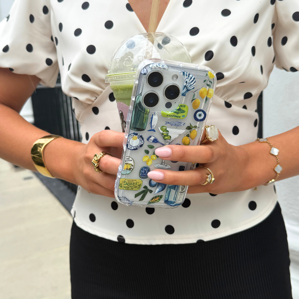 Woman with manicured nails holds an iced drink and a clear Coconut Lane phone case with Martini Coast design.