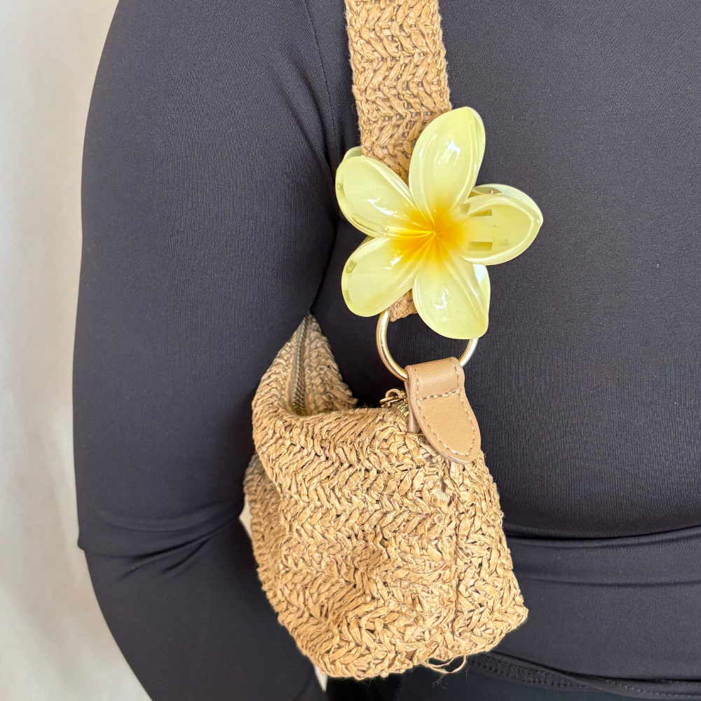 Woven straw bag with a large yellow flower keychain and a butter yellow tropical flower claw clip.