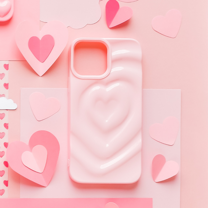 The Melting Heart Phone Case - Peony Pink by Coconut Lane is surrounded by various paper cutouts of pink and red hearts, clouds, and other decorations, all arranged on a pastel pink background.