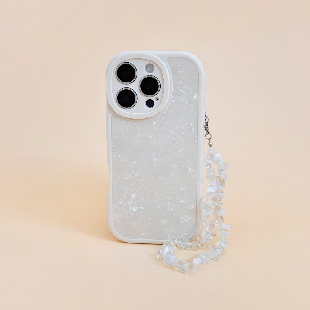 White iPhone with a pearlescent case and Coconut Lane Moonstone crystal phone strap on a light peach background.