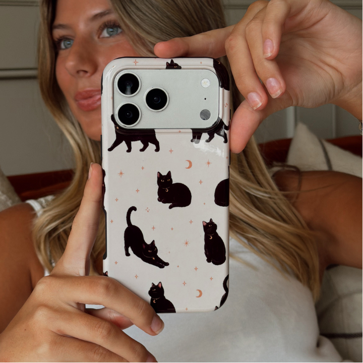 Woman holding up an iphone, showing a phone case with black cats printed on the case.