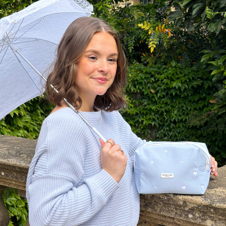 Girl posing by garden holding lace umbrella holding her Blue Hearts Makeup Bag