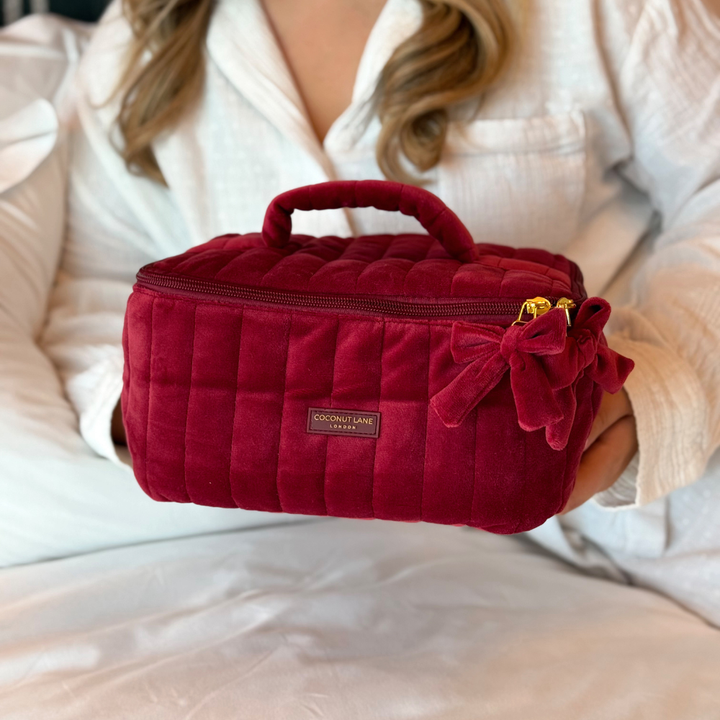girl in white Pjs holds Burgundy velvet cosmetic bag with a quilted design, top handle, bow detail, and gold-tone hardware.
