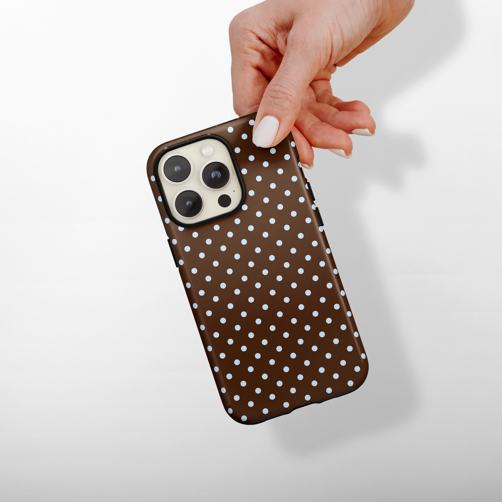 Hand holding Coconut Lane Tough Phone Case with brown and blue polka dot pattern on a white background.