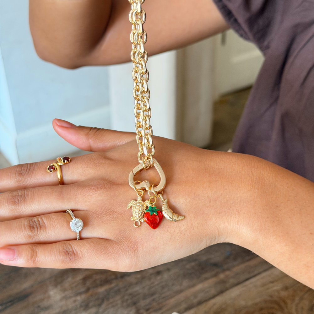 Gold Phone Strap with strawberry charm on a wrist, with a neutral background