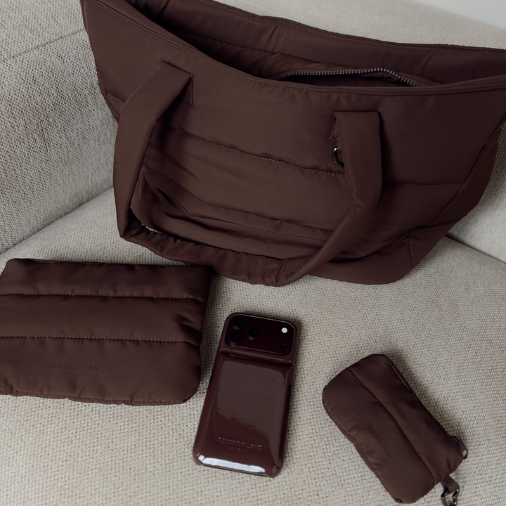 Chocolate brown puffer collection featuring a mini keyring bag with zip fastening, silver metal heart shaped clip, a Choc puffer everything pouch and the matching chocolate brown puffer phone case, all with the Coconut Lane logo. 