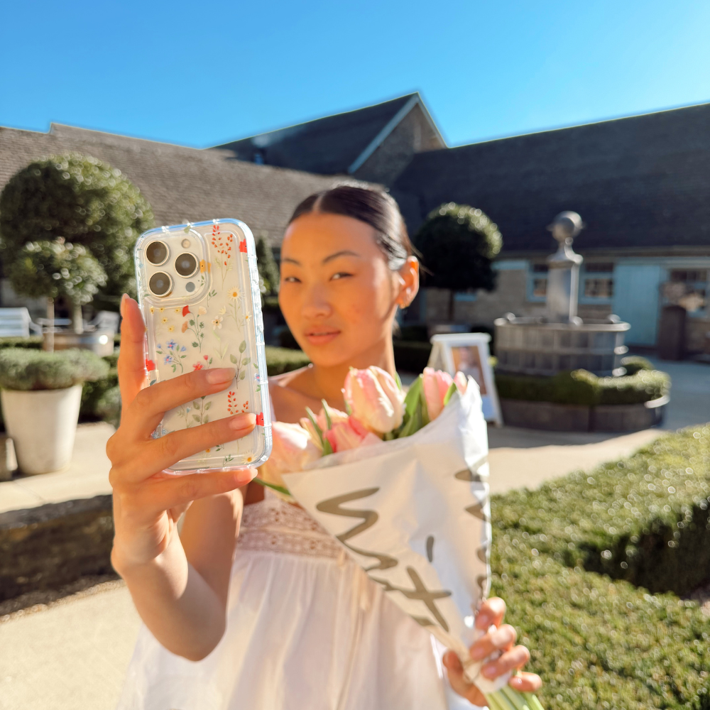 Girl taking a selfie with her Colourful Wildflower Phone Case next to a bunch of pretty pink flowers