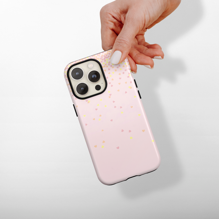 Hand holding a pink phone case with small colourful hearts on a light gray background