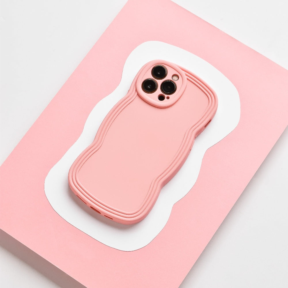 A strawberry-colored smartphone with a matching wavy-edged case rests on a pink and white abstract-patterned surface. The matte finish of the Coconut Lane NAKD Curvy Phone Case - Strawberry adds an elegant touch, while its highly protective design ensures the three-lens rear camera setup remains safe and secure.