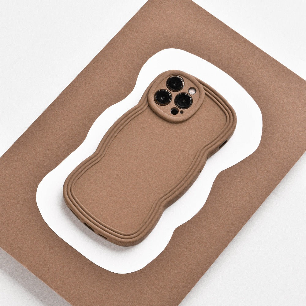 A lightweight, brown NAKD Curvy Phone Case - Coffee from Coconut Lane with a wavy design lies on a flat, brown and white, wavy-edged surface. The case has precise cutouts for the camera lenses and appears highly protective. The background contrasts with the NAKD Curvy Phone Case, highlighting its unique shape and design.