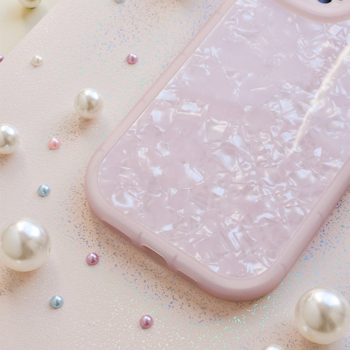 A Moonstone Pink Phone Case from Coconut Lane with a pearlescent, mosaic-like design placed on a glittery pink surface. Surrounding the protective phone case are scattered pearls of varying sizes, adding a touch of elegance to the scene.