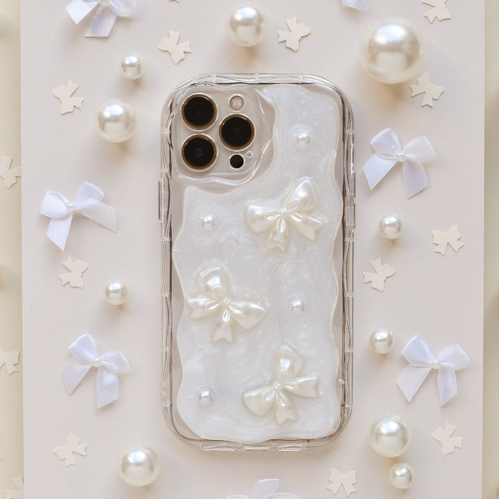 The Pearls & Bows Phone Case by Coconut Lane showcases a protective design adorned with iridescent white fabric, featuring elegant pearl-like bows and beads. The background is accentuated with petite, white bow-shaped ornaments and scattered pearl-like decorations, perfectly enhancing the sophisticated and delicate theme of this iPhone15 case.