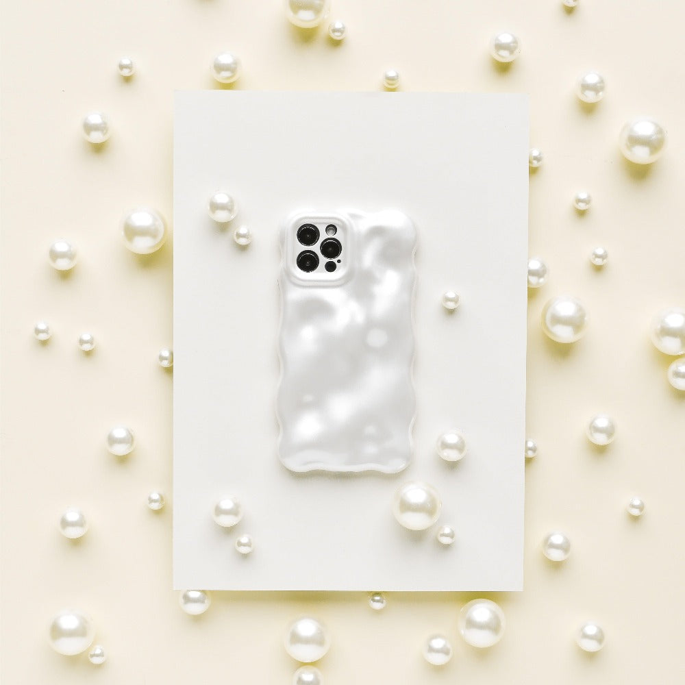 A Coconut Lane 3D Pearl Phone Case in white, featuring a glossy, wavy, pearl effect, is placed on a white rectangular sheet. The sheet is surrounded by various sizes of white pearls scattered on a light beige surface, creating an elegant and sophisticated display.
