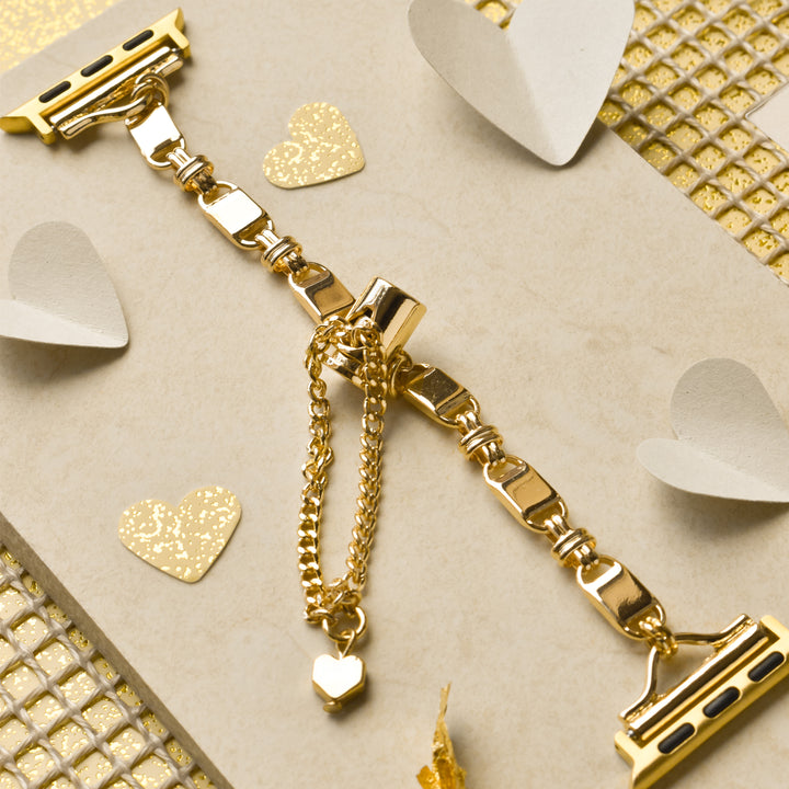 The Simple Gold Bracelet Apple Watch Strap by Coconut Lane, showcased on a beige card adorned with gold and white heart cutouts, features a delicate chain with a heart charm. The elegant presentation is complemented by a gold, grid-patterned background.
