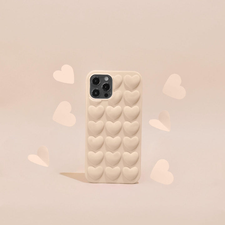 A 3D Hearts Phone Case - Matte Nude by Coconut Lane is displayed on a matching beige background, perfectly fitting the iPhone15's three camera lenses. Surrounding the case are several scattered heart shapes, enhancing its cohesive and charming aesthetic.