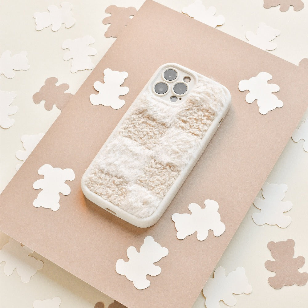 A Cosy Teddy Phone Case in Vanilla Biscuit by Coconut Lane is placed on a beige sheet of paper. Surrounding the phone are small, white bear-shaped cutouts scattered on a cream-colored surface, creating a cozy and whimsical scene.