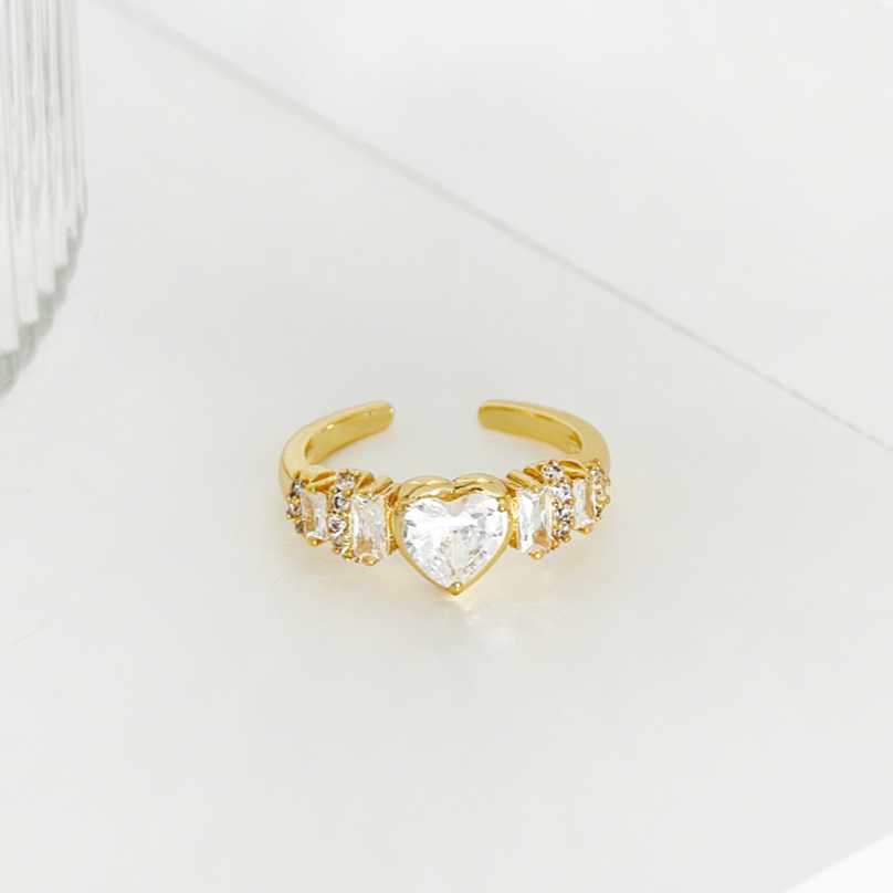 Gold adjustable heart ring with diamante center and side stones, displayed on a white background.