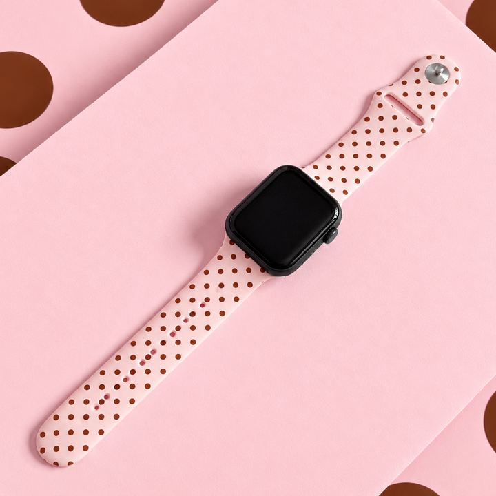 Pale pink silicone sport band with small brown polka dots, attached to a black Apple Watch smartwatch.