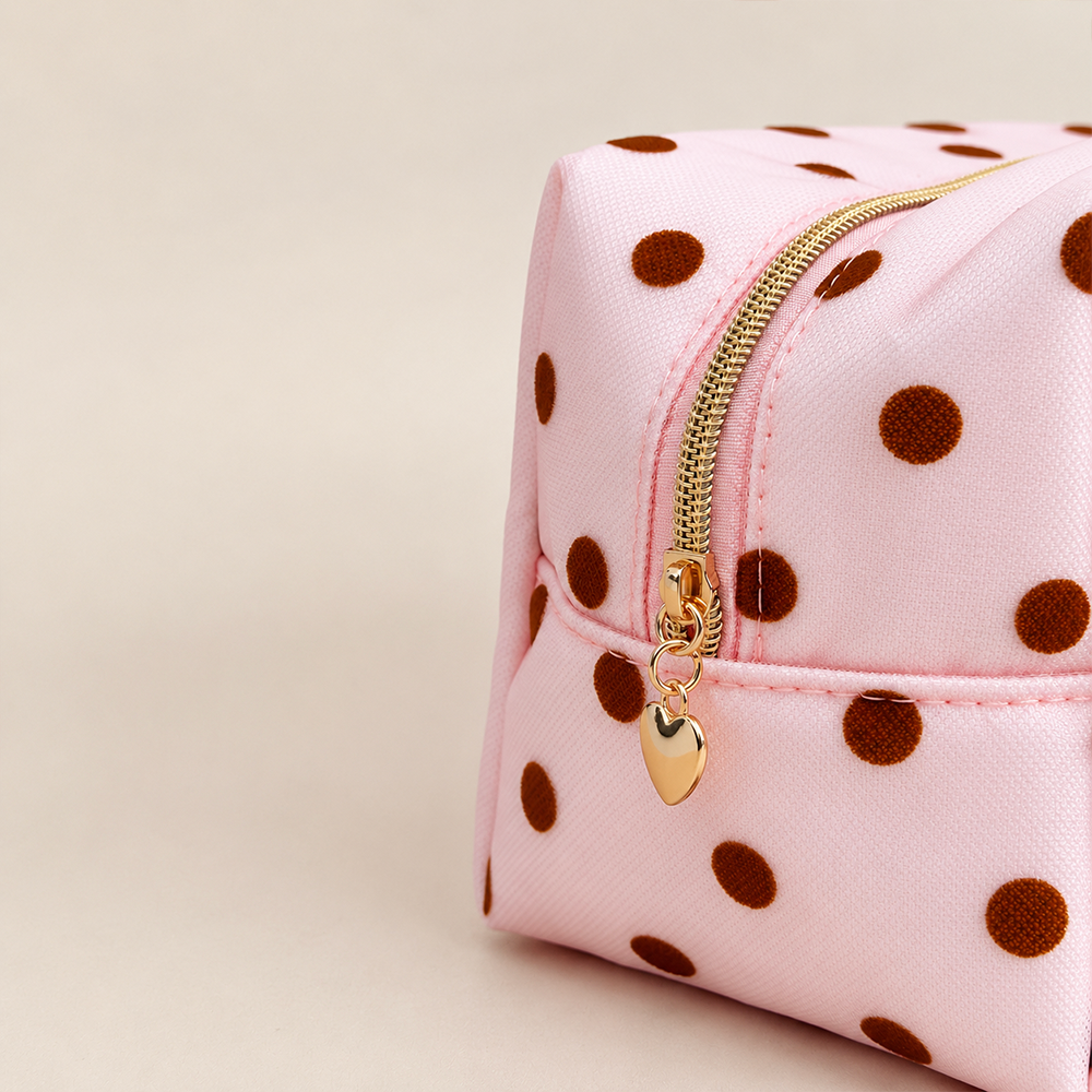 Close-up of pnk mesh makeup bag with brown polka dots and a gold top zip with a heart-shaped zip pull.