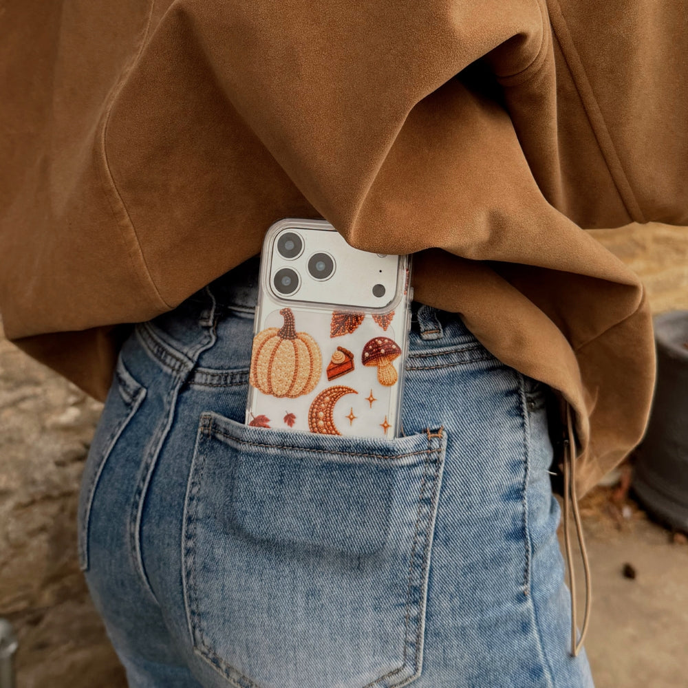 A person wearing a brown suede jacket and light blue jeans, shown from the back. With the Fall for It Clear Case decorated with autumn-themed beaded effect designs including pumpkins, acorns, mushrooms, leaves, and a pumpkin spice coffee cup, tucked into the back pocket
