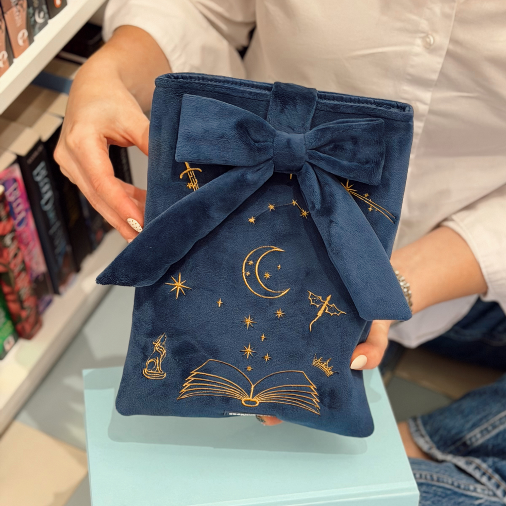 Book Sleeve made from soft navy blue velvet with gold embroidered crescent moon, stars, crown and open book illustrations, finished with a large velvet bow and Coconut Lane logo.