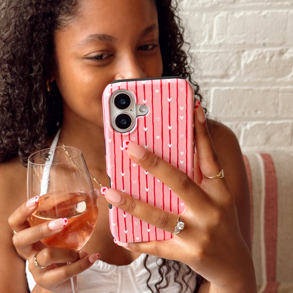 Woman holding a glass and a phone with a pink striped case with hearts.
