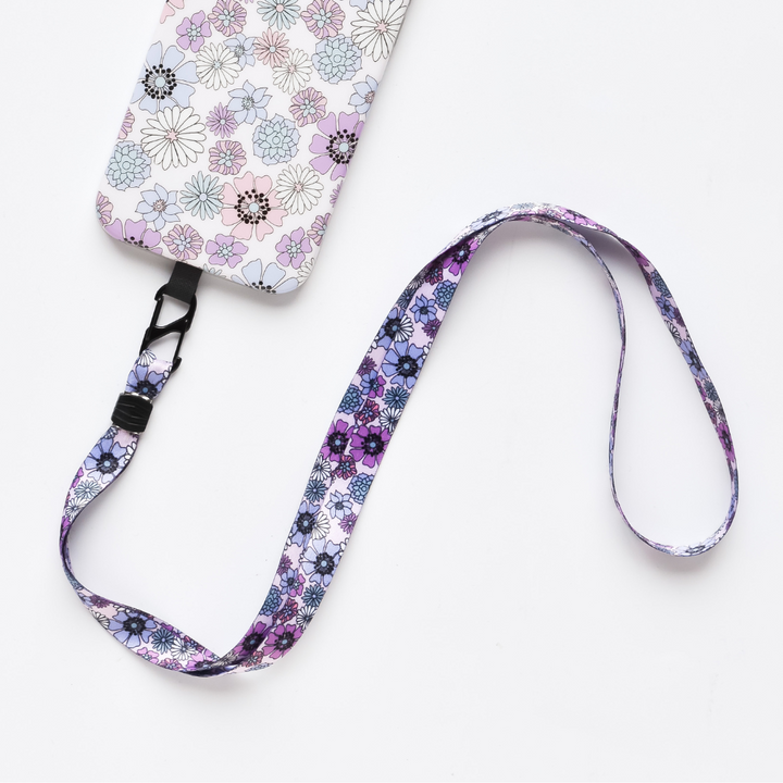 The Universal Phone Lanyard Patch Bundle by Coconut Lane includes an attached cardholder adorned with a pastel-colored floral pattern, featuring flowers in pink, white, and light purple. The lanyard mirrors this beautiful design in shades of purple and black on a white background—perfect for enhancing your phone's security.