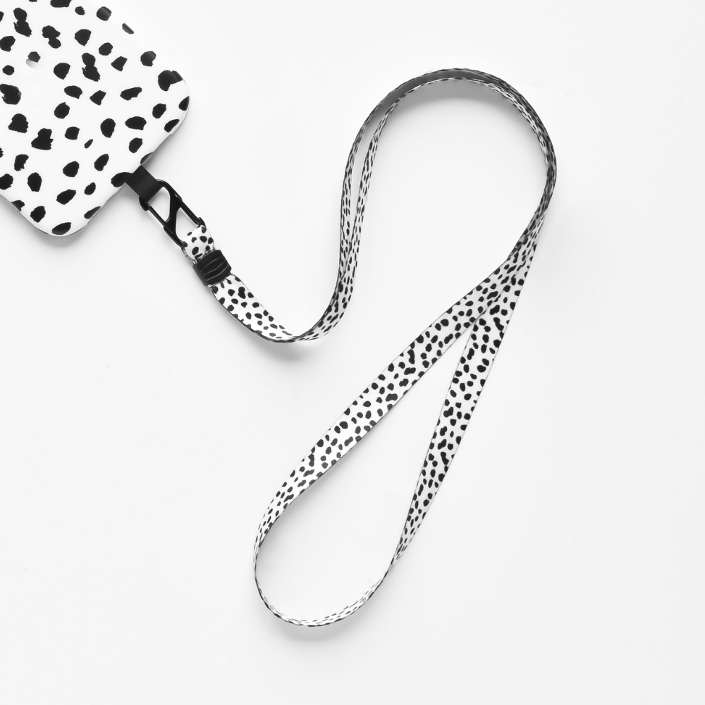 A black-and-white lanyard with a Dalmatian-like spotted pattern from Coconut Lane is laid out on a white surface. This Universal Phone Lanyard Patch Bundle features an attached rectangular cardholder with the same spotted design, offering both style and phone security.