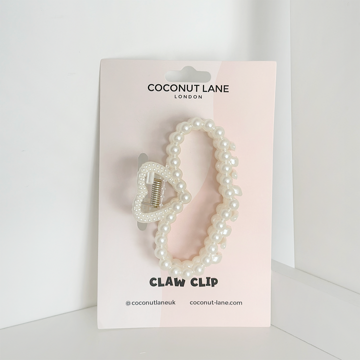 A chic addition to your collection, the Pearl Heart Claw Clip from Coconut Lane is adorned with pearl beads and attached to a light pink display card featuring white lettering. The card showcases the brand's name and social media handle "@coconutlaneuk".