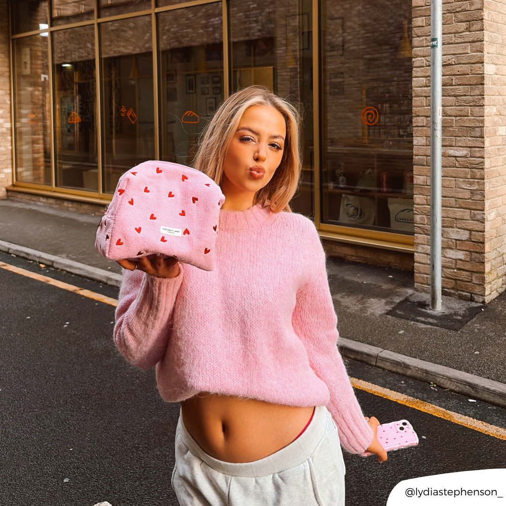 Girl in street in pink jumper matching a pink heart makeup bag