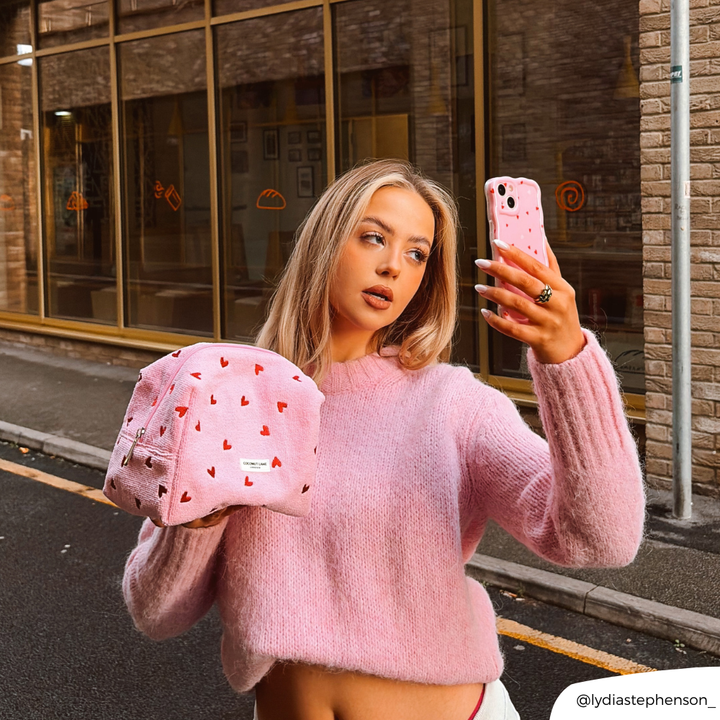 Girl taking selfie with cute hearts phone case whilst holding pink hearts makeup bag