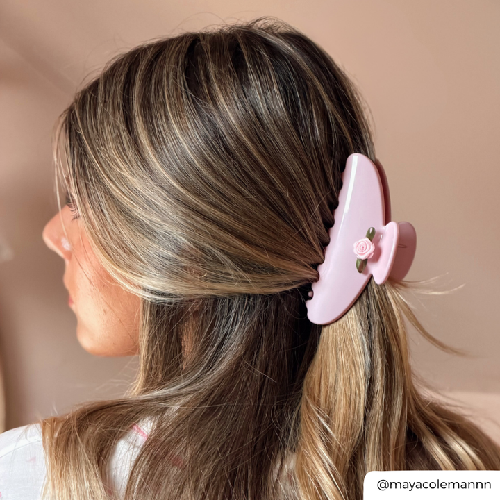 A woman shown from the side wearing a light pink hair claw clip holding back her hair. The claw clip has a pin rose on it.