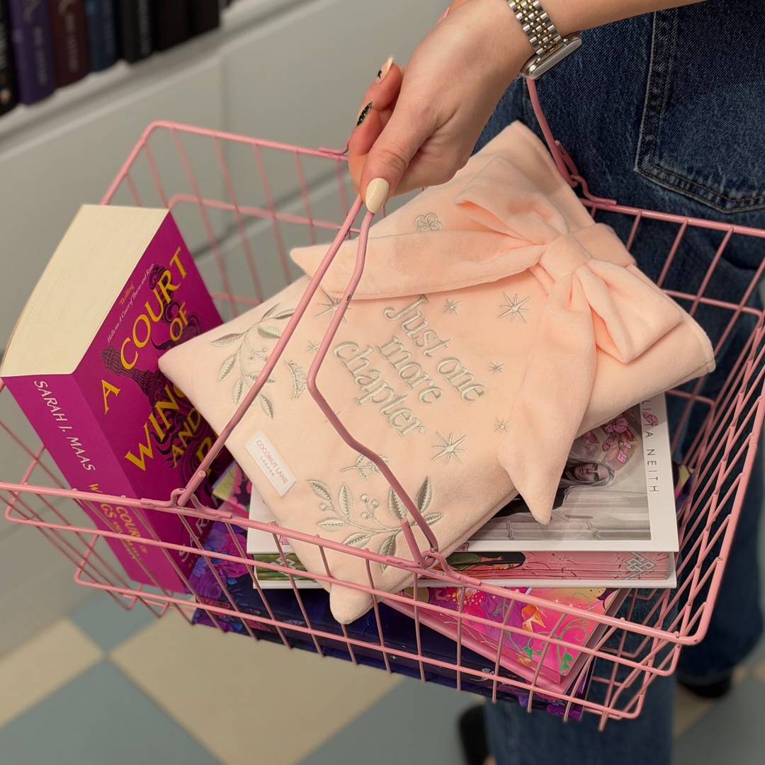 Book Sleeve made from soft blush pink velvet with grey embroidered floral details, stars and 'Just One More Chapter' lettering, finished with a large pink velvet bow and Coconut Lane logo, 
