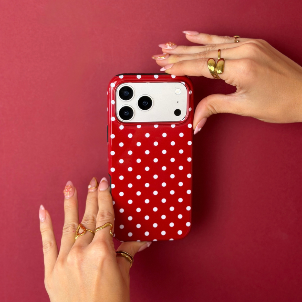 Woman holding an iphone with a red and white polka dot phone case. Woman is accessorised with gold jewellery. 
