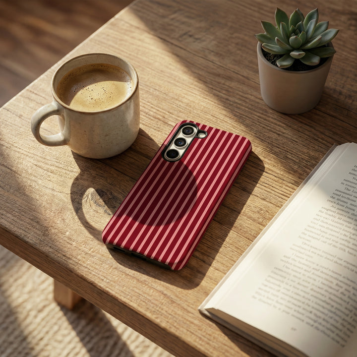 Red striped phone case on a wooden table with a cup of coffee, book, and plant.