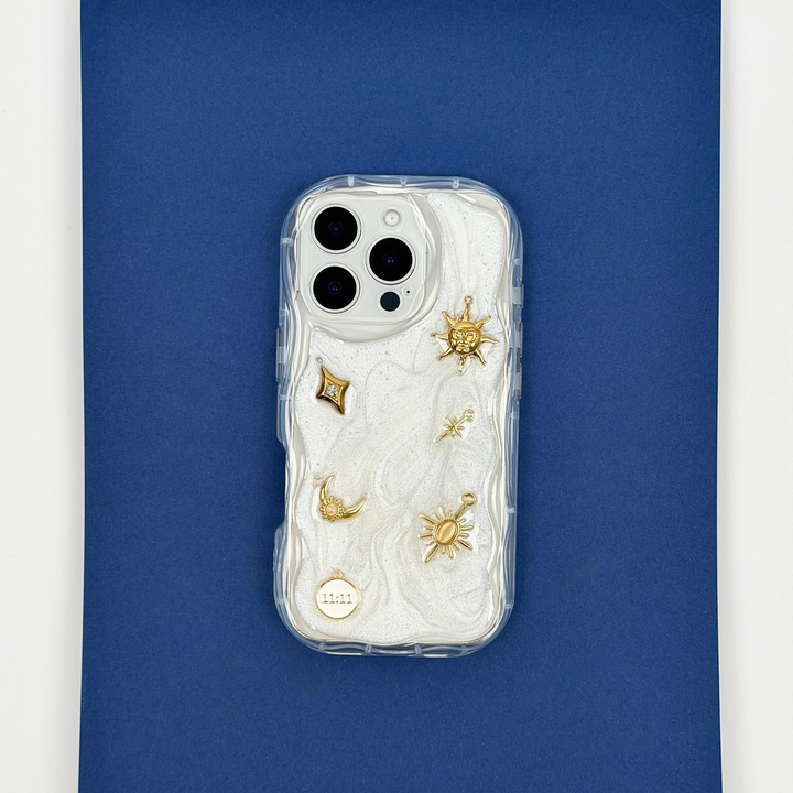 Stardust after dark charm phone case. A pearl base with luxe gold celestial charms including a moon, sun, star, diamond shape and 11:11 charm. 