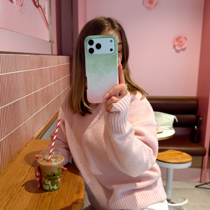 A girl sat in a cafe wearing a pink jumper taking a selfie with Tough Phone Case Strawberry Matcha
