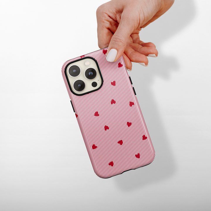 Phone case with red heart pattern held by a hand on a light gray background
