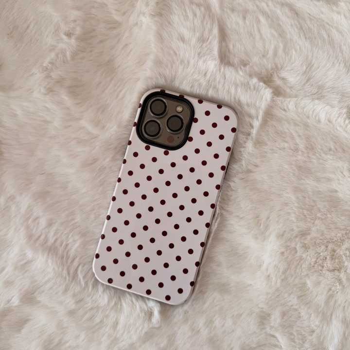 Iphone placed on a white fluffy rug. Phone is in a cream case with brown polka dots. 