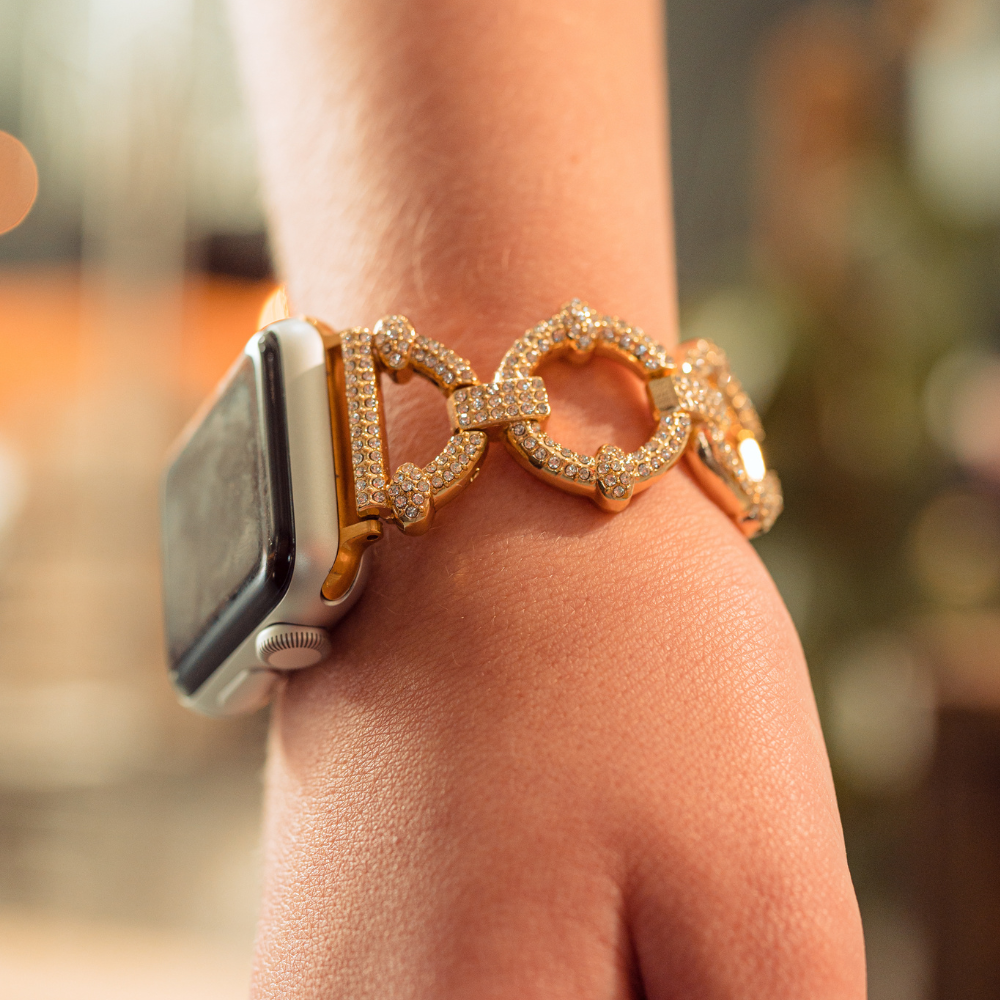 Close-up of a person's wrist adorned with the Coconut Lane Diamante Bracelet Apple Watch Strap, which features sparkling gemstones. The band showcases large circular links, enhancing the elegance of the accessory. The background is blurred, emphasizing the bracelet.
