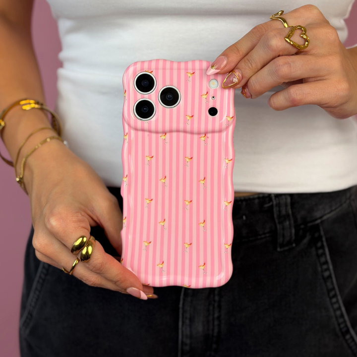 A wavy pink striped phone case with small spicy margarita illustrations, held by a person wearing a white top and black jeans against a solid pink background.